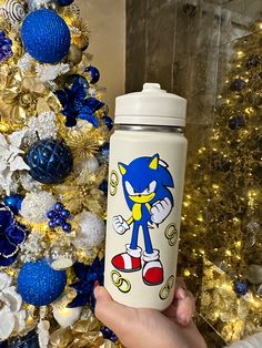 someone is holding a water bottle in front of a christmas tree with gold and blue decorations