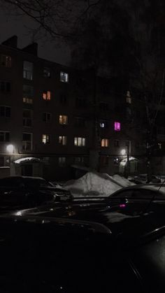 cars parked in the snow at night with buildings lit up behind them and street lights on