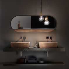 a bathroom with two sinks under a mirror and lights hanging above the sink, on top of a shelf