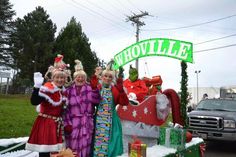 three women dressed up in costumes standing next to a christmas float with presents on it