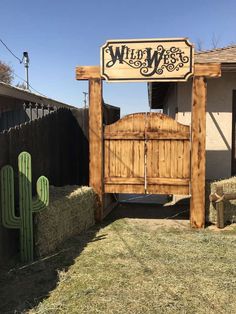 a wooden gate with a sign that says wild west in front of a house and cactus