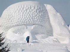 a man standing in front of a giant snow sculpture that looks like a person's head