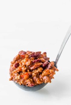 a bowl filled with chili and beans on top of a white table next to a spoon