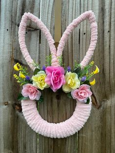 a knitted bunny ears wreath with flowers and greenery hanging on a wooden fence