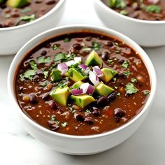 three white bowls filled with black bean chili and avocado garnished with cilantro