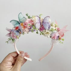 a hand is holding a flower crown with butterflies on the top and flowers in the middle