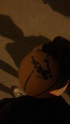 a person holding a basketball in their hand on the ground with shadows from people's feet