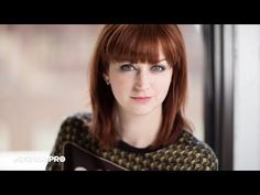 a woman with red hair and blue eyes is looking at the camera while standing in front of a window