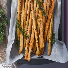 some bread sticks with herbs on them in a tray next to a fork and napkin