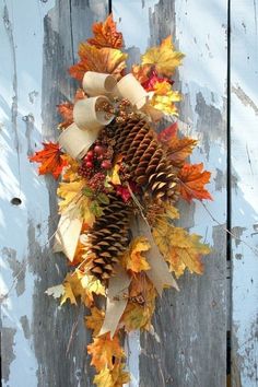 a wreath made out of pine cones and autumn leaves on a wooden fence with ribbon