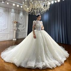 a woman in a wedding dress standing on a wooden floor next to a chandelier