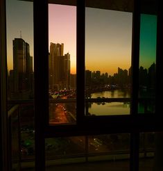 a window view of a city at sunset with the sun going down and buildings in the distance