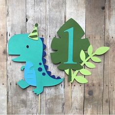 two dinosaur cupcake toppers with one number on them and the other decorated in green, blue and yellow