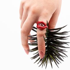 a woman's hand with a ring on it that has a red flower in the middle