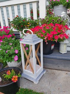 a white lantern sitting on top of a porch next to flowers and potted plants