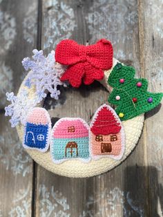 a crocheted christmas wreath with small houses and trees on it, sitting on top of a wooden table