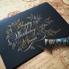 a black birthday card with gold lettering on it and a fountain pen next to it