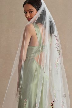 a woman wearing a veil and dress with flowers on the side is standing in front of a beige background