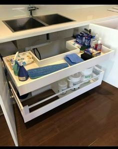 a kitchen sink under a counter with cleaning products and other items in the bottom drawer