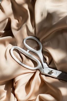 a pair of white scissors laying on top of a pink cloth covered in satin material