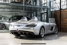 a silver sports car parked in a garage next to a white and black car with its doors open