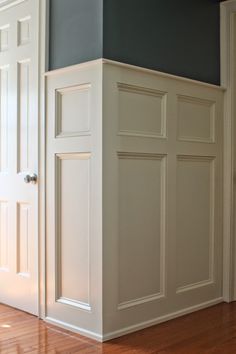 an empty room with white doors and hard wood flooring on one side, dark blue walls in the other