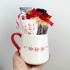 a hand holding a coffee mug filled with marshmallows and candy canes