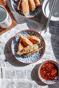 two plates filled with food on top of a newspaper next to cups and saucers