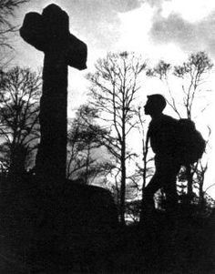 the silhouette of a man with a backpack is walking past a cross on a hill