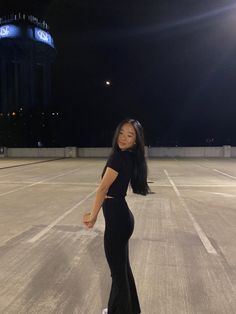 a woman standing in an empty parking lot at night with her hands on her hips