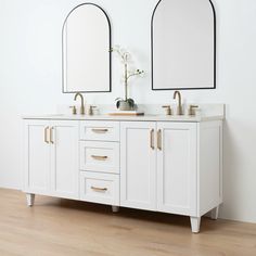 two mirrors are above the double sinks in this white bathroom with wood floors and wooden flooring