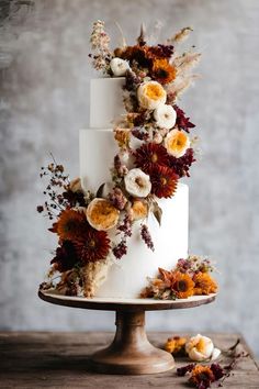 a three tiered white cake with flowers and foliage on the top is sitting on a wooden table