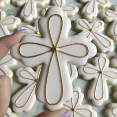 a person holding a white and gold cross cookie in front of some cookies on a table