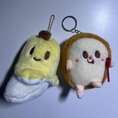 two stuffed animals are hanging from keychains on a white surface, one is yellow and the other is brown