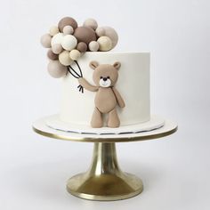 a teddy bear holding balloons on top of a white cake