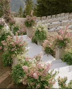 an outdoor wedding setup with white linen and pink flowers in planters on either side of the aisle