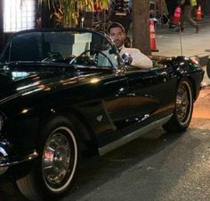 a man sitting in the driver's seat of an old fashioned black convertible car