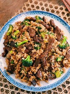 a blue and white plate topped with meat and broccoli covered in rice on top of a table