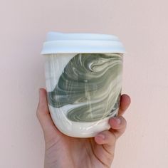 a hand holding a coffee cup with marbled design on the bottom and white lid