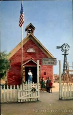 an old photo of people standing in front of a red building with a flag on top