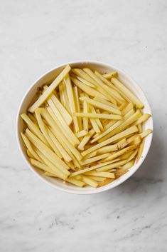 a white bowl filled with french fries on top of a marble counter