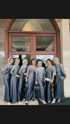 four women in grey dresses posing for a photo outside the door of a building with their hands on their hips