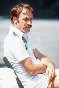 a man sitting on top of a bench next to a lake wearing a green tie