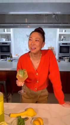 a woman sitting at a table holding a wine glass with lemons and other food on it