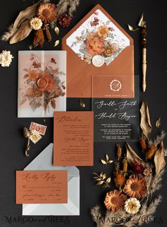 the wedding stationery is laid out on top of an orange and gray envelope, surrounded by dried flowers