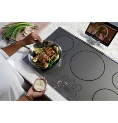 a woman is cooking food on the stove with her phone and laptop in the background