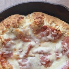 a pizza with ham and cheese in a cast iron skillet on a wooden table