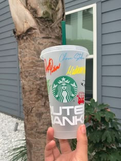 a hand holding up a starbucks cup in front of a tree