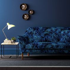 a living room with blue walls and palm print couch next to a small end table