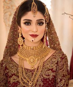 a woman in a red and gold bridal outfit with jewelry on her neck, wearing a